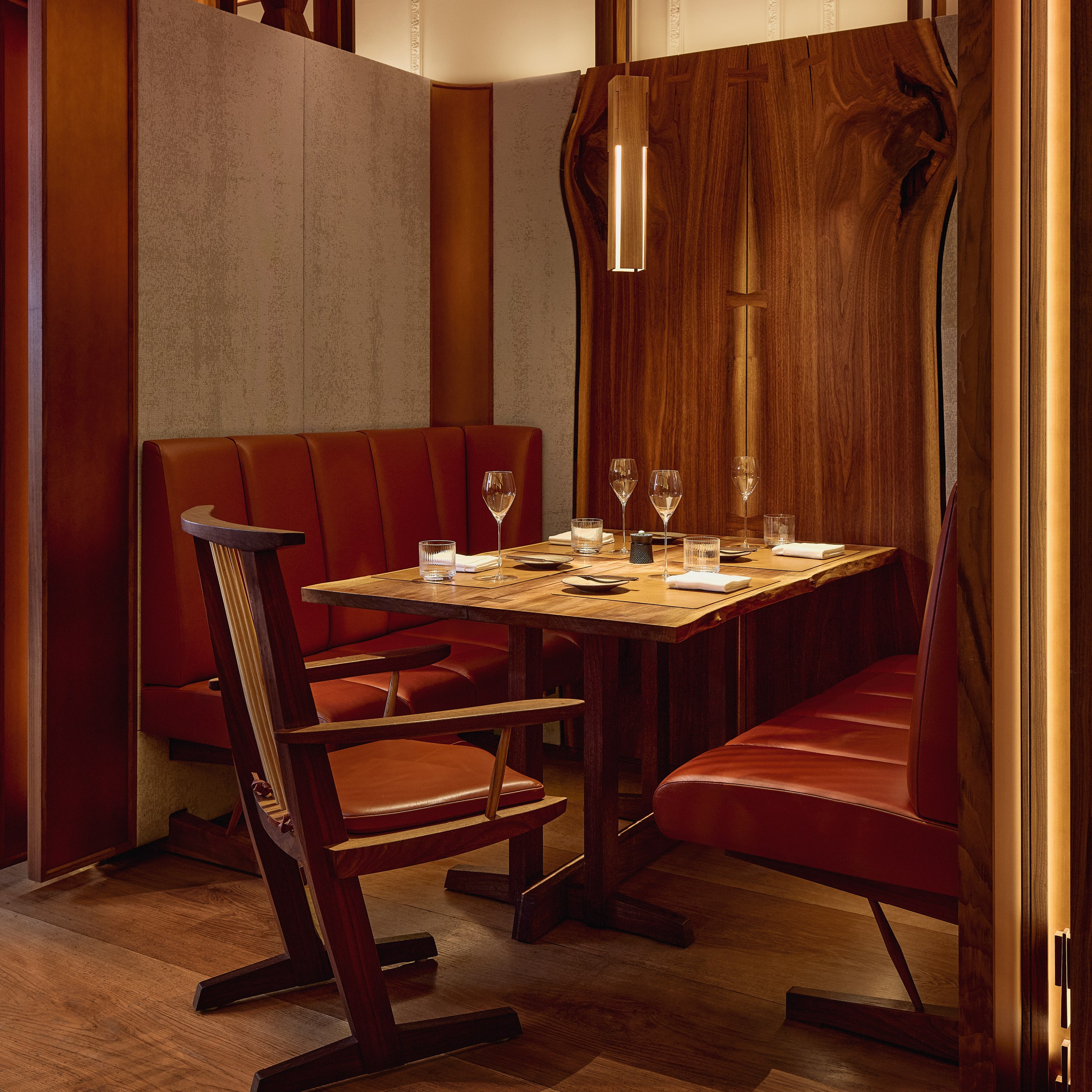 Intimate dining booth at The Connaught Grill, with caramel-toned leather banquettes, a polished wood table, and contemporary pendant lighting, framed by natural timber panelling.