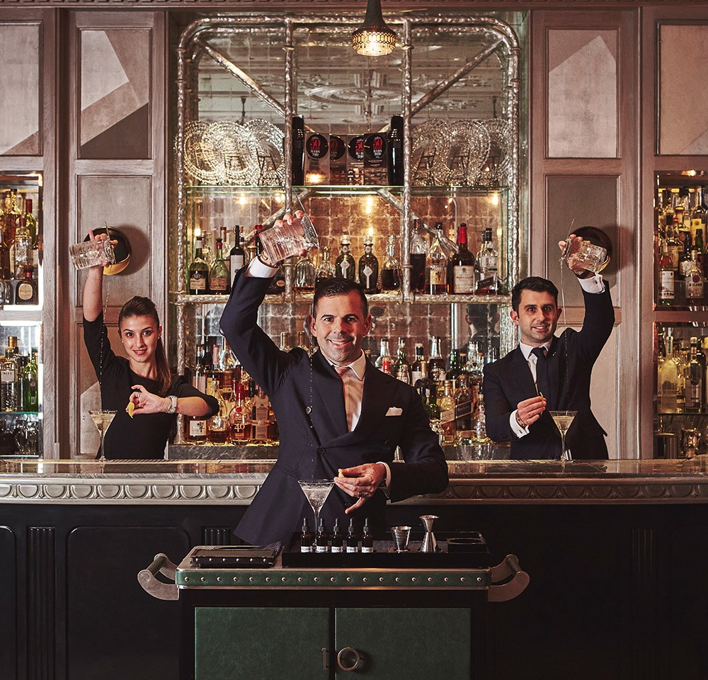 Three mixologists preparing drinks at The Connaught Bar, surrounded by the timeless elegance of the interior.