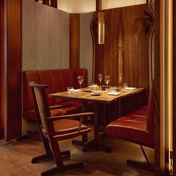 Intimate dining booth at The Connaught Grill, with caramel-toned leather banquettes, a polished wood table, and contemporary pendant lighting, framed by natural timber panelling.