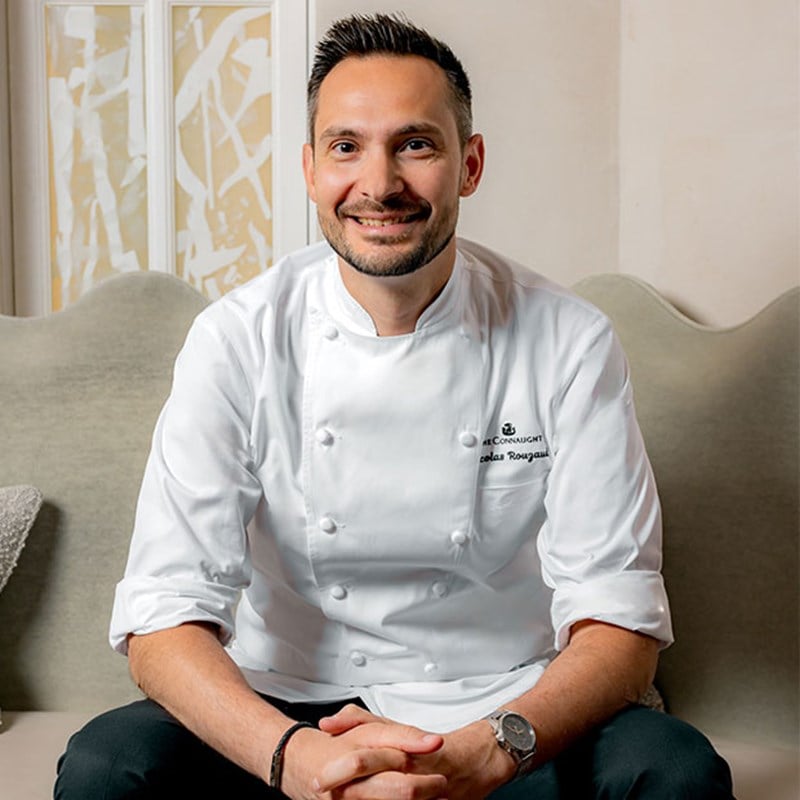 Image portrait of Nicolas Rouzaud in branded chef's white, sat down smiling.