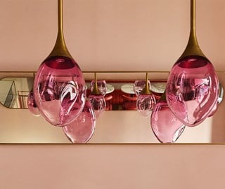 Close-up of sculptural pink glass pendant lights hanging from a ceiling, reflected in a mirrored wall behind.