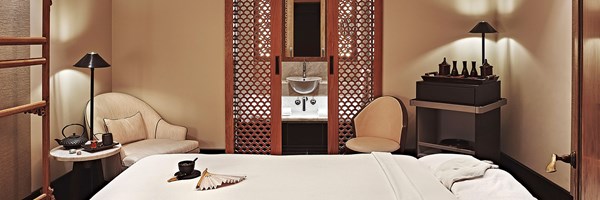 Aman Spa Treatment bed in foreground with a fan placed on it, in a cosy treatment room setting with tea, spa products and a bath in the background