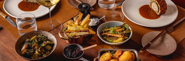 A festive meal spread showcasing a beautifully plated poultry dish, roasted vegetables, and an assortment of sides, set on a wooden table with elegant place settings.