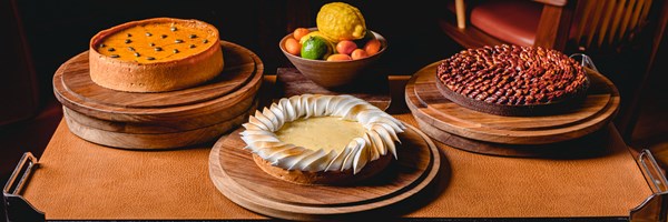 A decadent display of seasonal tarts, including a pumpkin pie, lemon meringue, and nut tart, alongside a bowl of fresh citrus fruits.