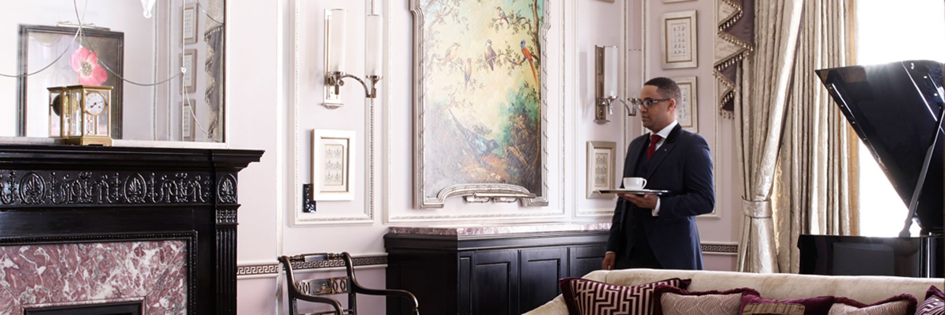 butler holding tray with coffee cup placed on top in luxurious hotel suite with a grand piano, fireplace and in the living room