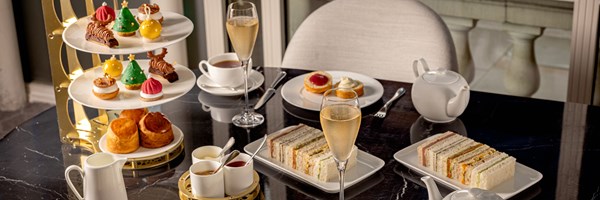 A lavish afternoon tea setup featuring festive pastries, scones, sandwiches, tea, and champagne on a marble table at The Connaught.