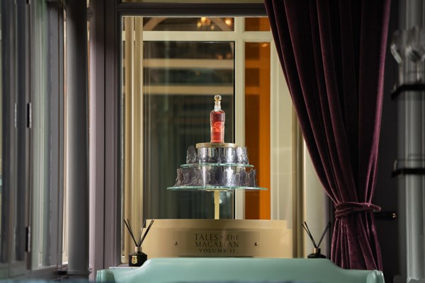 A bottle of 'Tales of The Macallan Volume II is elegantly displayed on a multi-tiered stand in the Coburg Bar, with burgundy curtains behind.