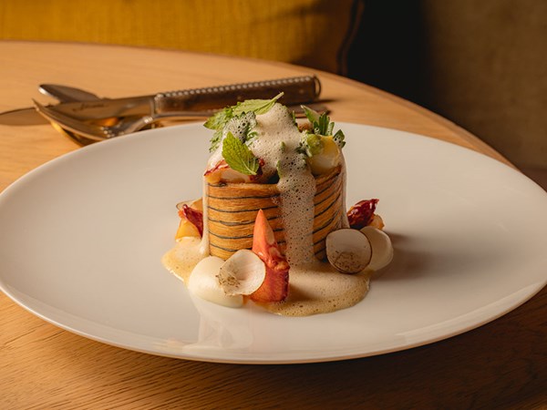 A beautifully assembled vol-au-vent filled with seafood, garnished with herbs and topped with a light foam, alongside delicate vegetable accompaniments.