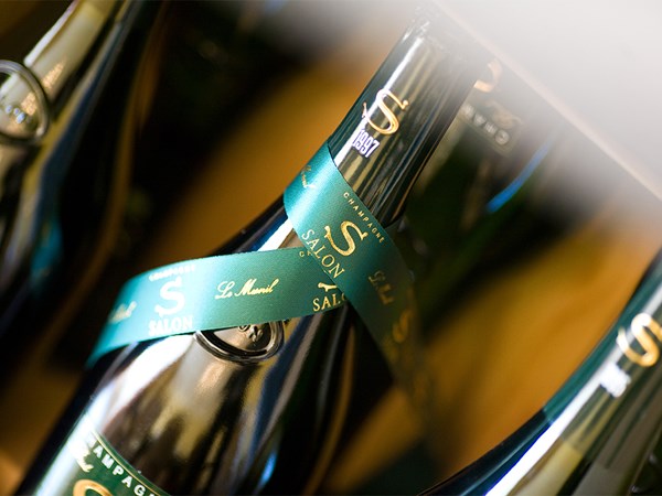 Elegant bottles of Champagne Salon, marked with signature green ribbons, are displayed in a refined setting, highlighting their exclusivity and prestige.