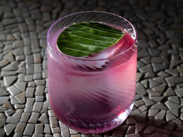 Pink / purple cocktail in short ribbed glass with green garnish