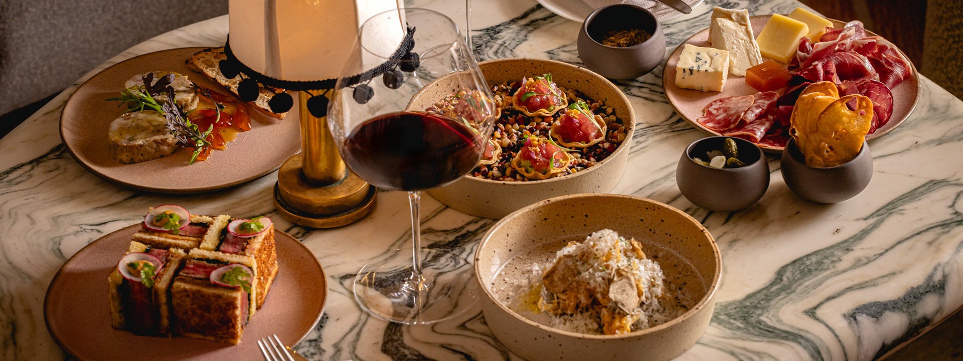 A luxurious spread of gourmet dishes, including charcuterie, salads, and truffle pasta, elegantly arranged on a marble table with a glass of red wine.