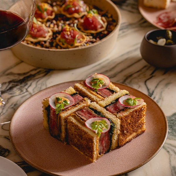 A close-up of a plate with Wagyu katsu sandwiches garnished with radish and greens, accompanied by vibrant dishes in the background.