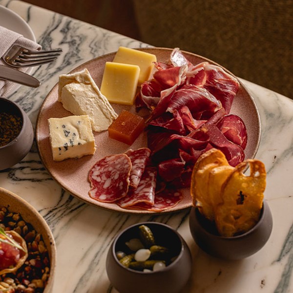 A charcuterie and cheese board artfully arranged with various cheeses, cured meats, and accompaniments on a marble table.