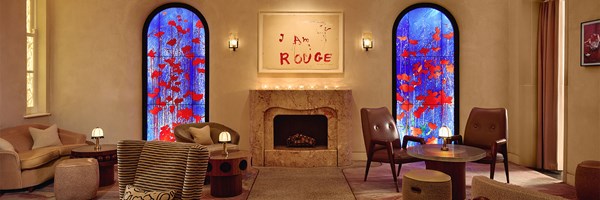 The Red Room lounge at The Connaught, featuring a central marble fireplace flanked by vivid blue stained-glass artworks with red poppies, soft ambient lighting, and contemporary seating in warm neutral tones.