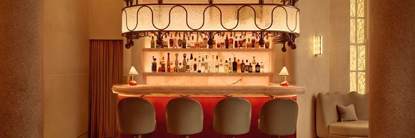 Curved marble bar at The Red Room, softly illuminated and backed by a glowing display of fine spirits, with sculptural overhead lighting and elegant, plush bar stools in a warm, tonal setting.