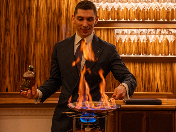 A dapper host flambées with Aberfeldy whisky, creating a dramatic culinary moment in a luxurious, warmly lit setting.