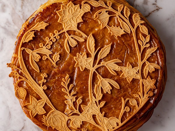 A golden-brown galette des rois with intricate floral and botanical pastry decorations adorning its surface.