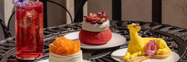 3 different Connaught Patisserie creations including a yellow cake shaped like a connaught hound with sunglasses, a red cake with whipped cream and orange whipped cream cake, and also a red juice garnished with berries and flowers.