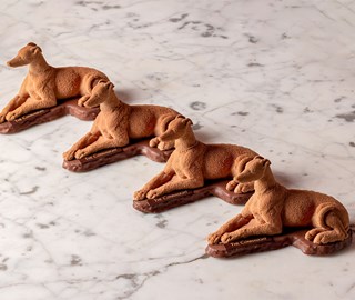 Row of four chocolate connaught patisserie hounds on a chocolate base. The hounds are positioned on a marble table.