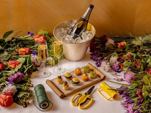 A refined tablescape featuring elegant canapés, flutes of champagne, and an ice bucket, surrounded by fresh, vibrant flowers and floral arranging tools.