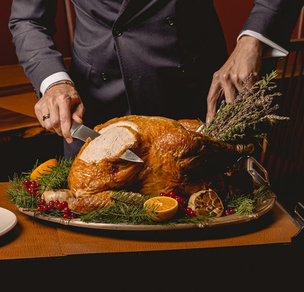 A finely carved golden roast turkey, garnished with fresh herbs, oranges, and cranberries, presented on a silver platter.