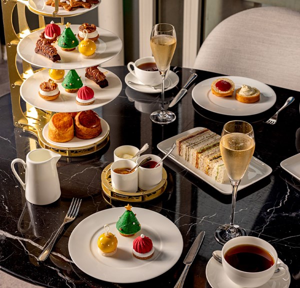 A luxurious festive afternoon tea spread featuring tiered desserts, scones, sandwiches, and glasses of champagne on a black marble table.