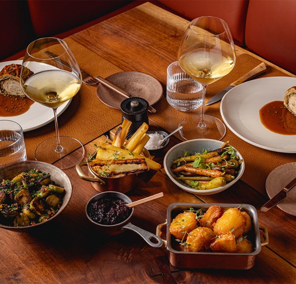 A decadent Christmas meal with elegantly plated side dishes, including roasted vegetables, potatoes, and glasses of white wine on a warm wooden table.