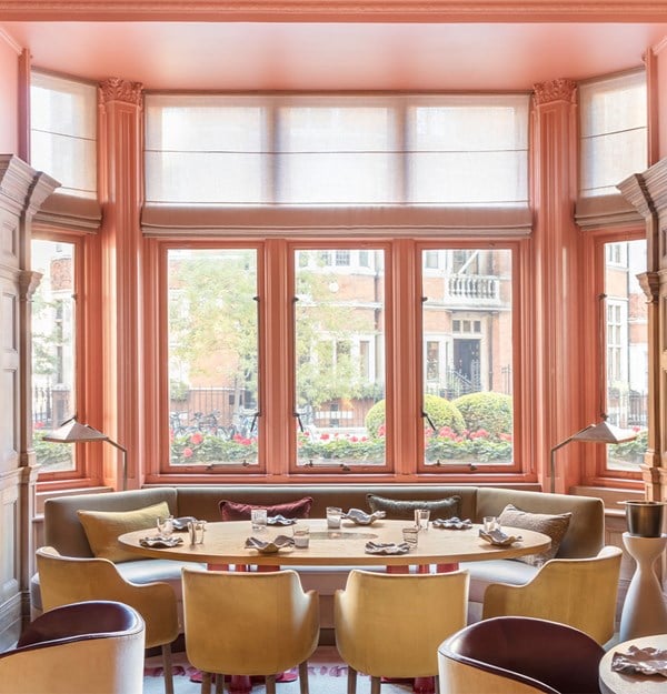 A sophisticated dining space with a large window, pastel tones, and a mix of modern and classic seating.