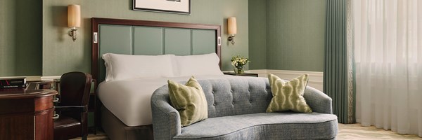 A serene and stylish guest room featuring a plush bed, a curved sofa, and calming green tones, exuding timeless elegance.