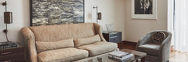 A cosy and elegant living room featuring a beige sofa, a grey armchair, framed artwork, and modern lighting fixtures with a glass coffee table in the centre.