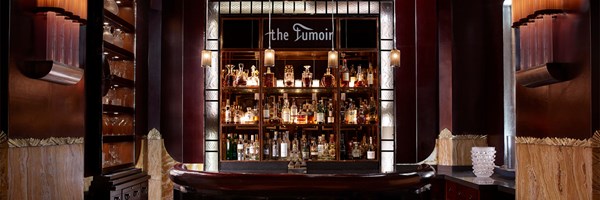 A luxurious bar with rich wooden tones, illuminated shelves filled with bottles, and an art deco aesthetic.