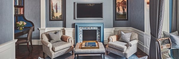 A sophisticated sitting area featuring plush armchairs, a charming fireplace with blue and white tile accents, and elegant artwork, framed by rich blue tones and classic furnishings that exude timeless luxury.