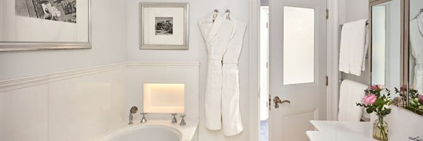 A bright, pristine bathroom exuding timeless elegance with plush white robes, a gleaming bathtub, and refined accents, perfect for indulgent relaxation.