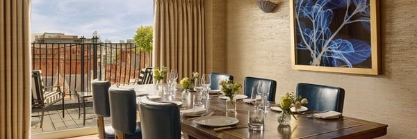 Private dining room with a polished table set for eight, opening onto a sunlit terrace with views across Mayfair’s rooftops.