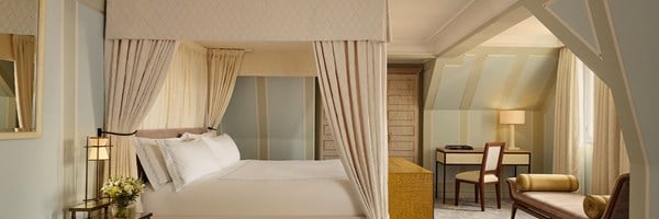 Charming attic bedroom with a curtained four-poster bed, soft pastel palette, and tailored furnishings beneath sloped ceilings.