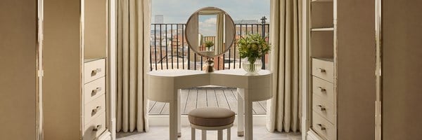 Elegant dressing space featuring a sculptural vanity and circular mirror, framed by mirrored wardrobes and opening to a rooftop terrace.