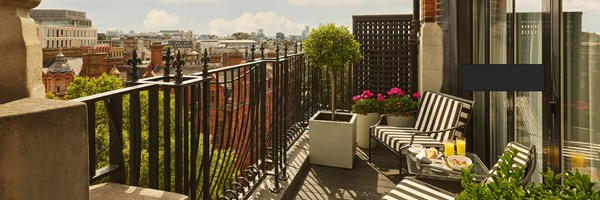 Chic rooftop terrace with striped loungers, manicured topiary, and a breakfast table set against sweeping London skyline views.